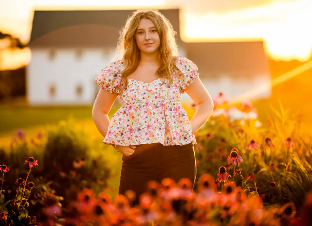 igh school senior girl posing outdoors at sunset in flowers in OwatonnaMinnesota, with warm golden light in the background during a senior portrait session.