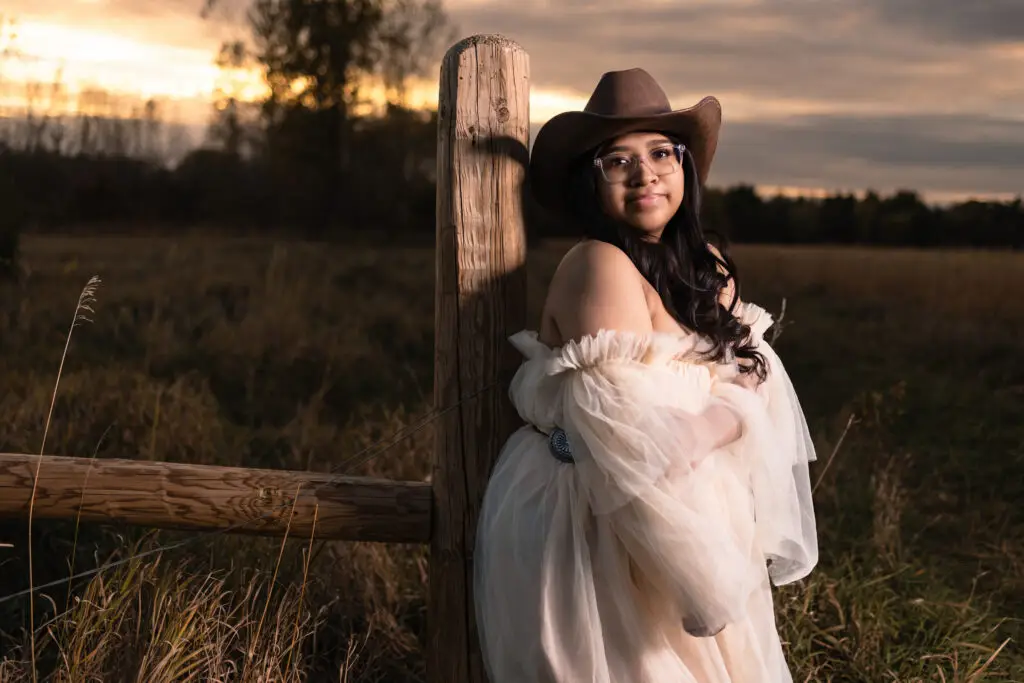 Female high school senior wearing a cowboy hat and posing outdoors at sunset in Owatonna, Minnesota, during a country-themed senior portrait session.