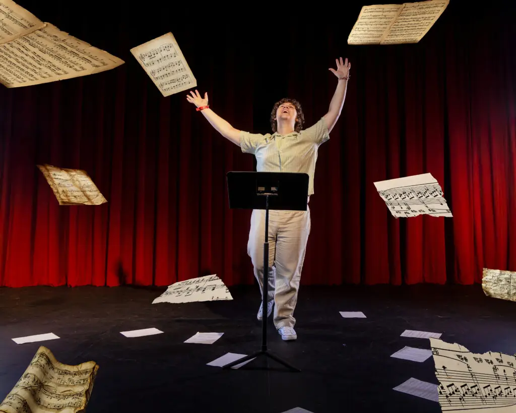 Male high school senior tossing sheet music into the air inside Owatonna Little Theatre in Minnesota during a senior portrait session.