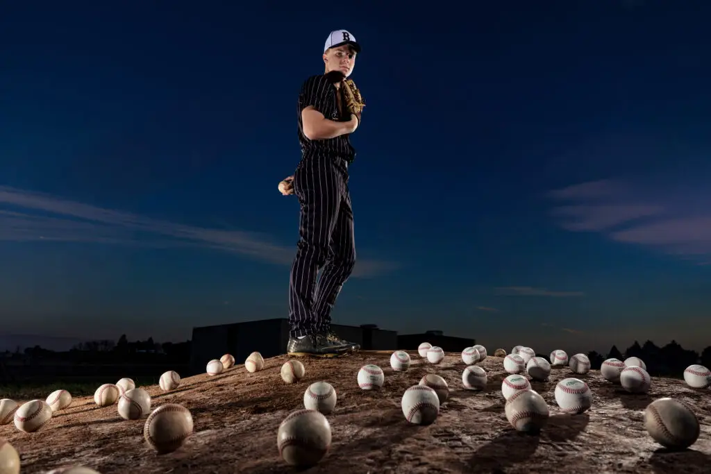 Male high school senior baseball pitcher posing on a pitching mound with baseballs around him during a senior portrait session in Blooming Prairie, Minnesota.