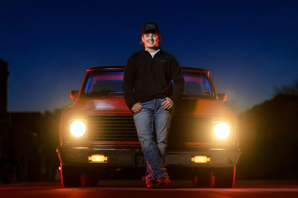 Male high school senior posing next to a red Chevy truck in downtown Blooming Prairie, Minnesota, during a senior portrait session.